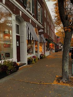 an empty street in front of a store with autumn leaves on the ground and parked cars