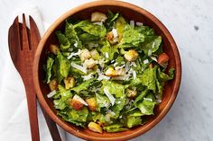 a wooden bowl filled with lettuce and croutons on top of a table