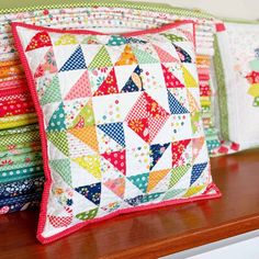 colorful pillows are stacked on top of each other in front of a wooden shelf with green and white wallpaper