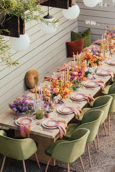 a long table is set with pink and yellow plates, green chairs, and floral centerpieces