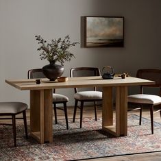 a dining room table with chairs and a vase on the rug in front of it