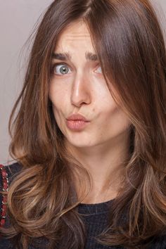 a woman with long brown hair and blue eyes looks at the camera while wearing a black sweater