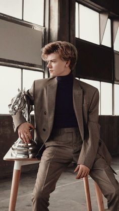 a young man sitting on top of a wooden chair next to a horse head statue