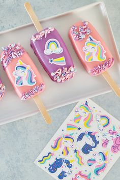 three popsicles with unicorns on them are sitting on a tray next to some stickers