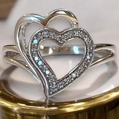 two heart shaped rings sitting on top of a gold ring stand with white and blue stones