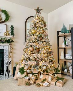 a christmas tree with presents under it and gold ornaments on the top, in front of a fireplace