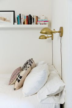 a white bed topped with lots of pillows next to a book shelf filled with books