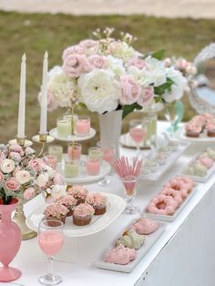 a table topped with pink and white cupcakes next to vases filled with flowers