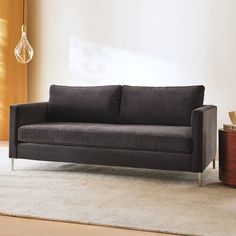 a black couch sitting on top of a white rug next to a wooden table and lamp