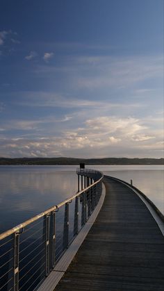 a long wooden pier stretches out into the water at dusk, with clouds in the sky