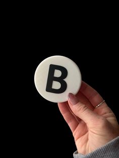 a person holding up a button with the letter b on it in front of a black background