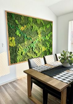 a dining room table with a large moss wall hanging above it and a checkered placemat on the table