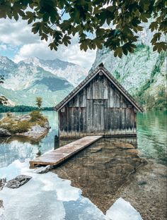 an old wooden house sitting on top of a body of water next to a mountain range