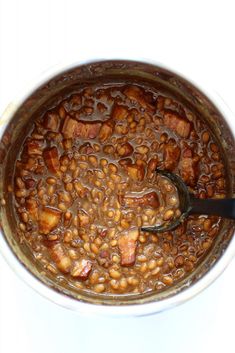 a pot filled with beans and meat on top of a white counter next to a spoon