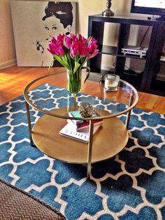 a glass coffee table with flowers on it in a living room area next to a blue rug