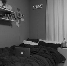 an unmade bed with a laptop on it in front of a book shelf and bookshelf