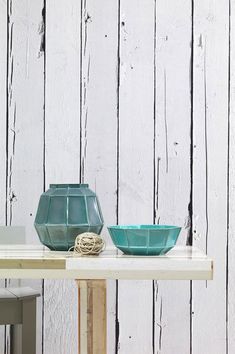 a table with two bowls on it next to a white wall and a blue vase