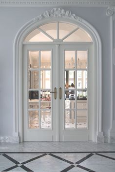 two white double doors in an ornately decorated room with marble flooring and black and white checkered tile