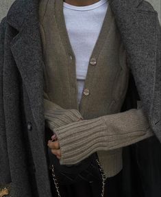 a woman wearing a gray sweater and black pants with her hands in her pockets,