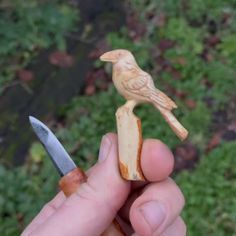 a small wooden bird sitting on top of a piece of wood next to a knife