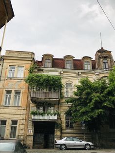 two cars are parked in front of an old building with ivy growing on the balconies