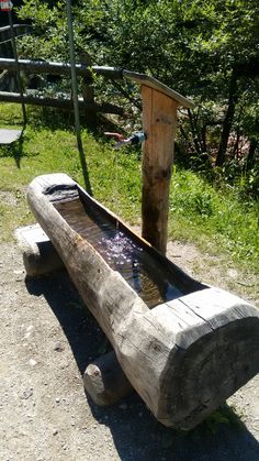 a wooden bench sitting on top of a dirt field next to a tree stump with water running down it