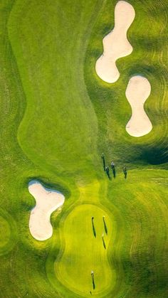 aerial view of golf course with green grass and white bunkers in the distance, taken from above