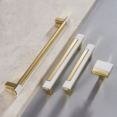 two handles, one with gold and the other white are next to each other on a marble countertop