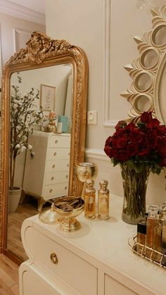 a white dresser topped with a vase filled with red roses next to a gold framed mirror