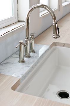 a white sink sitting under a window next to a counter top with two faucets