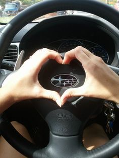 a person is making a heart shape with their hands on the steering wheel while driving