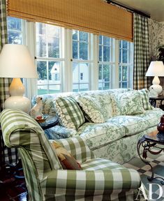 a living room filled with furniture next to two lamps and large windows covered in plaid curtains