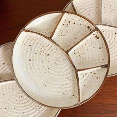 three white dishes with brown speckles on them sitting on a wooden table top