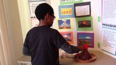 a young boy standing in front of a display with pictures on the wall and writing on it