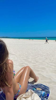 a woman sitting on top of a blue and white towel in front of the ocean