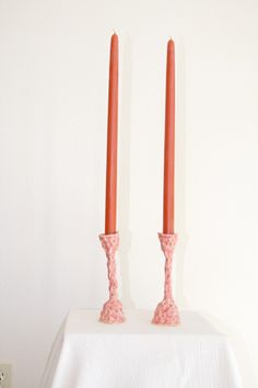 two candles are placed on top of a white table cloth and one is red with pink flowers