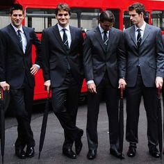 four men in suits and ties are holding umbrellas near a red double decker bus