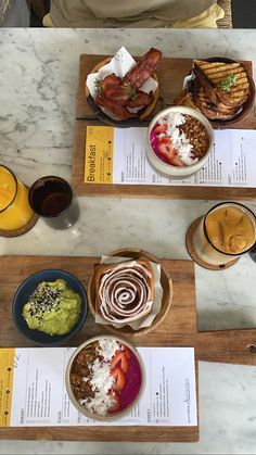 three plates of food on wooden trays with drinks and papers sitting on the table