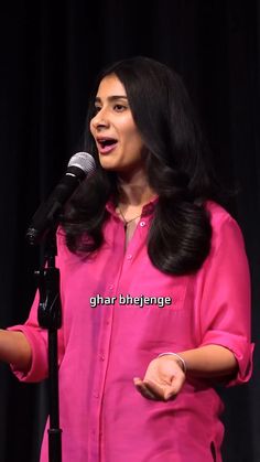 a woman standing in front of a microphone with her hands out and speaking into the microphone