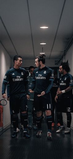 three soccer players are talking to each other in the locker room while others look on