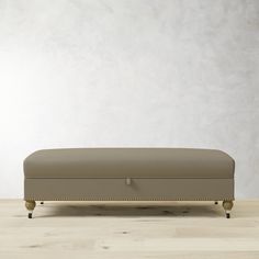 an upholstered footstool in front of a white wall and wooden floor