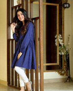 a woman standing in front of a wooden door wearing white pants and a blue dress