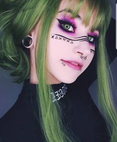 a woman with green hair and makeup has cat eye make up on her face,