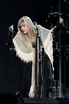 a woman with long blonde hair and fringed shawl on stage