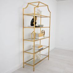 a gold shelf with books and other items on it, against a white wall in an empty room