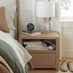 a nightstand with books and slippers on it next to a lamp in a bedroom