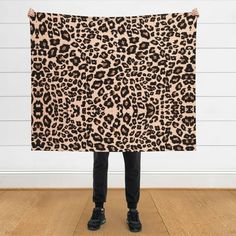 a person holding up a leopard print blanket in front of a white wall and wooden floor