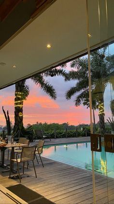 an outdoor dining area next to a swimming pool at dusk with palm trees in the background