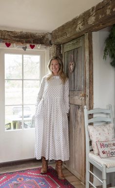 a woman standing in front of a wooden door wearing a white dress and brown boots