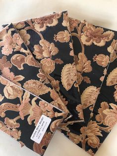 four pieces of black and gold fabric with floral designs on the sides, each folded up to show a price tag